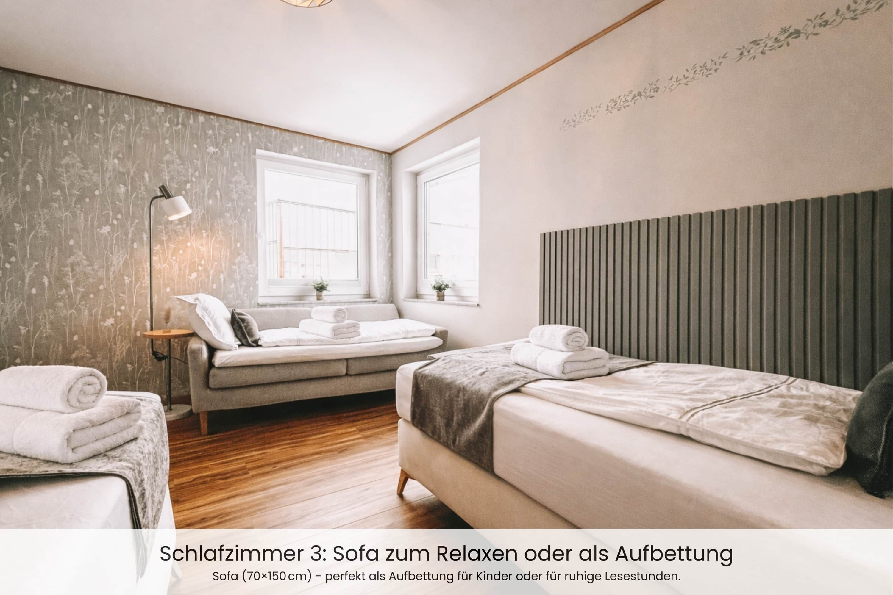 A bedroom with a sofa and a bed, both with neatly folded towels.