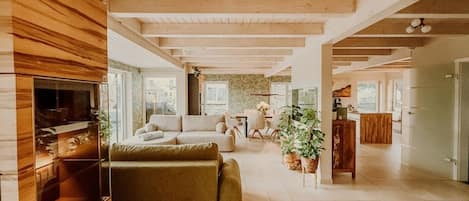 A spacious living area with a wooden ceiling, a sofa, a dining table, and a kitchen area.