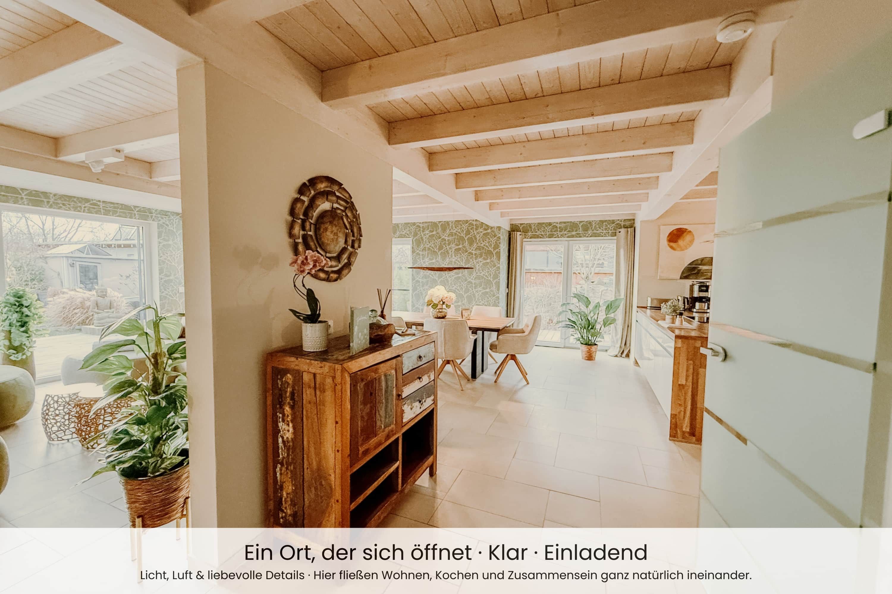 Ein geräumiger, gut beleuchteter Innenraum mit Holzbalkendecke, einer Essecke mit Tisch und Stühlen sowie einer Küchenzeile mit Arbeitsplatte und Schränken.