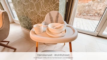 A high chair with a tray, a cup, and a bowl, positioned near a window with a view of a garden.