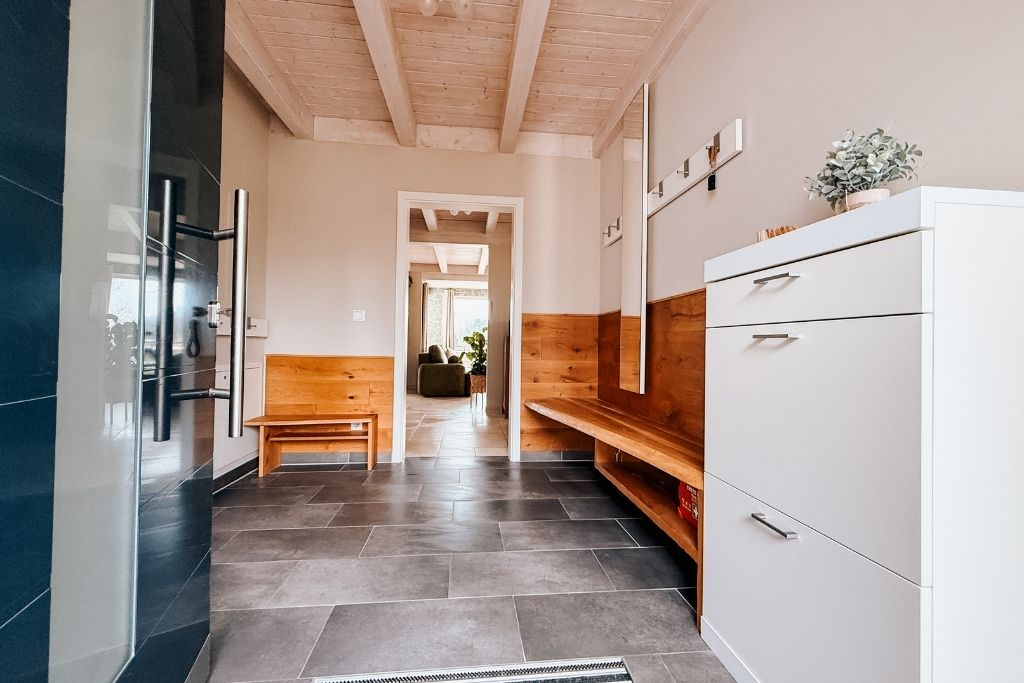 A modern kitchen with a wooden bench, white cabinetry, and a view into another room.