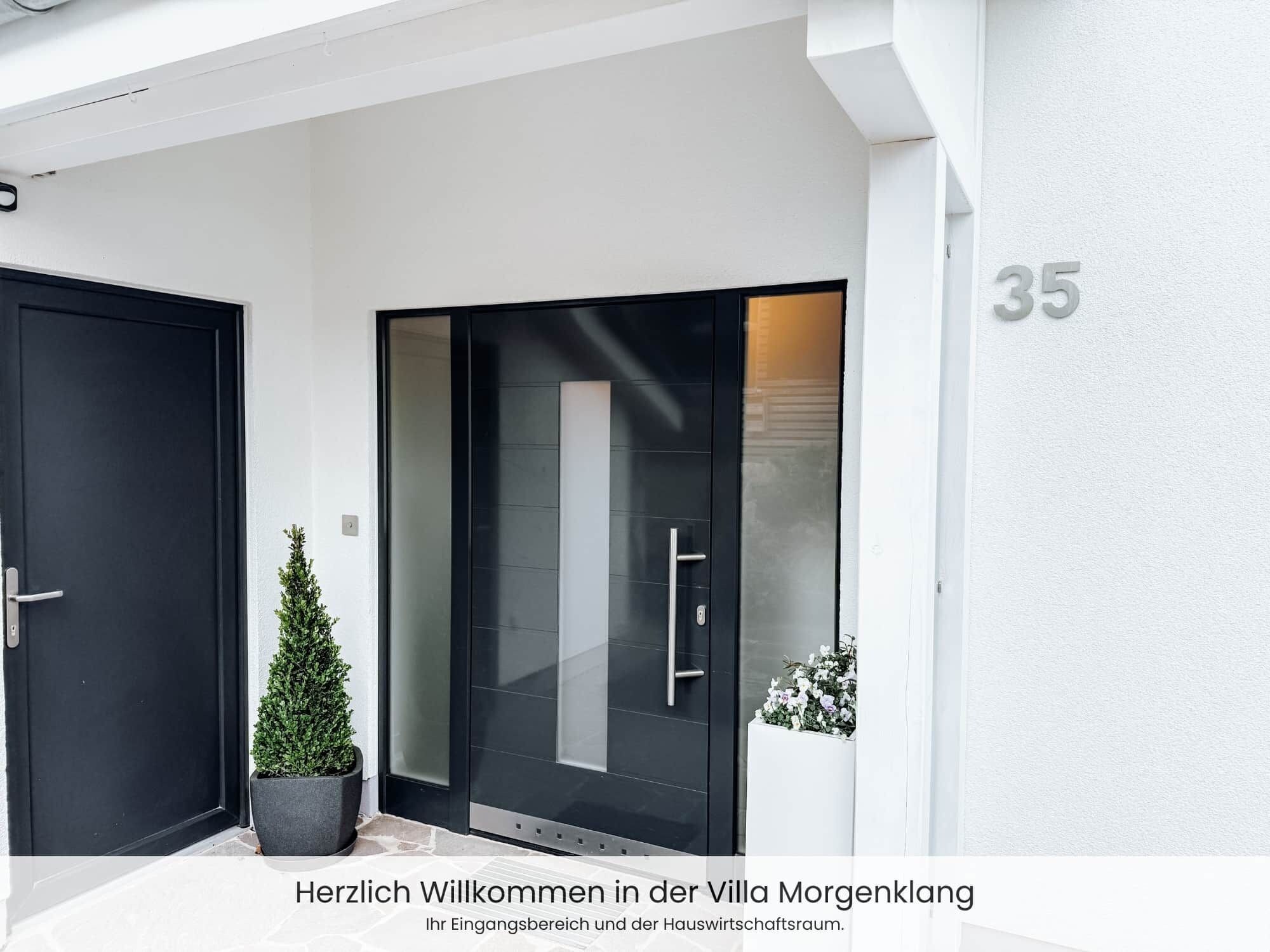 Ein moderner Villa-Eingang mit einer schwarzen Tür, einem Topf mit Pflanze und der Hausnummer 35 an der Wand.