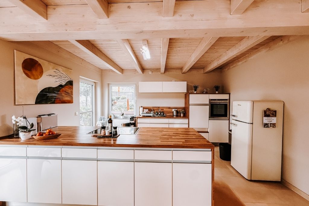 A modern kitchen with wooden beams, white cabinetry, and a central island.