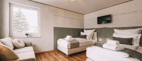 A modern hotel room with a bed, a sofa, a TV, and a window with a view of a tree.