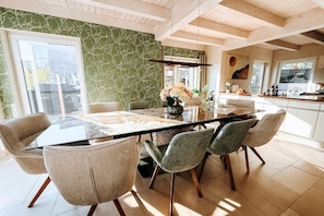 Un espace repas moderne avec une table en verre, six chaises et un mur orné d’un motif vert.