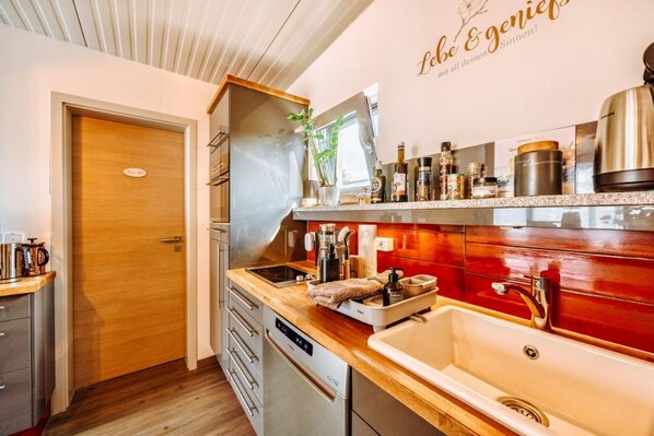 A modern kitchen with a wooden countertop, stainless steel appliances, and a red backsplash.