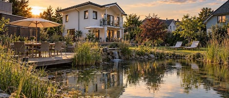 A lakeside property with a wooden deck, outdoor seating, and a pond.