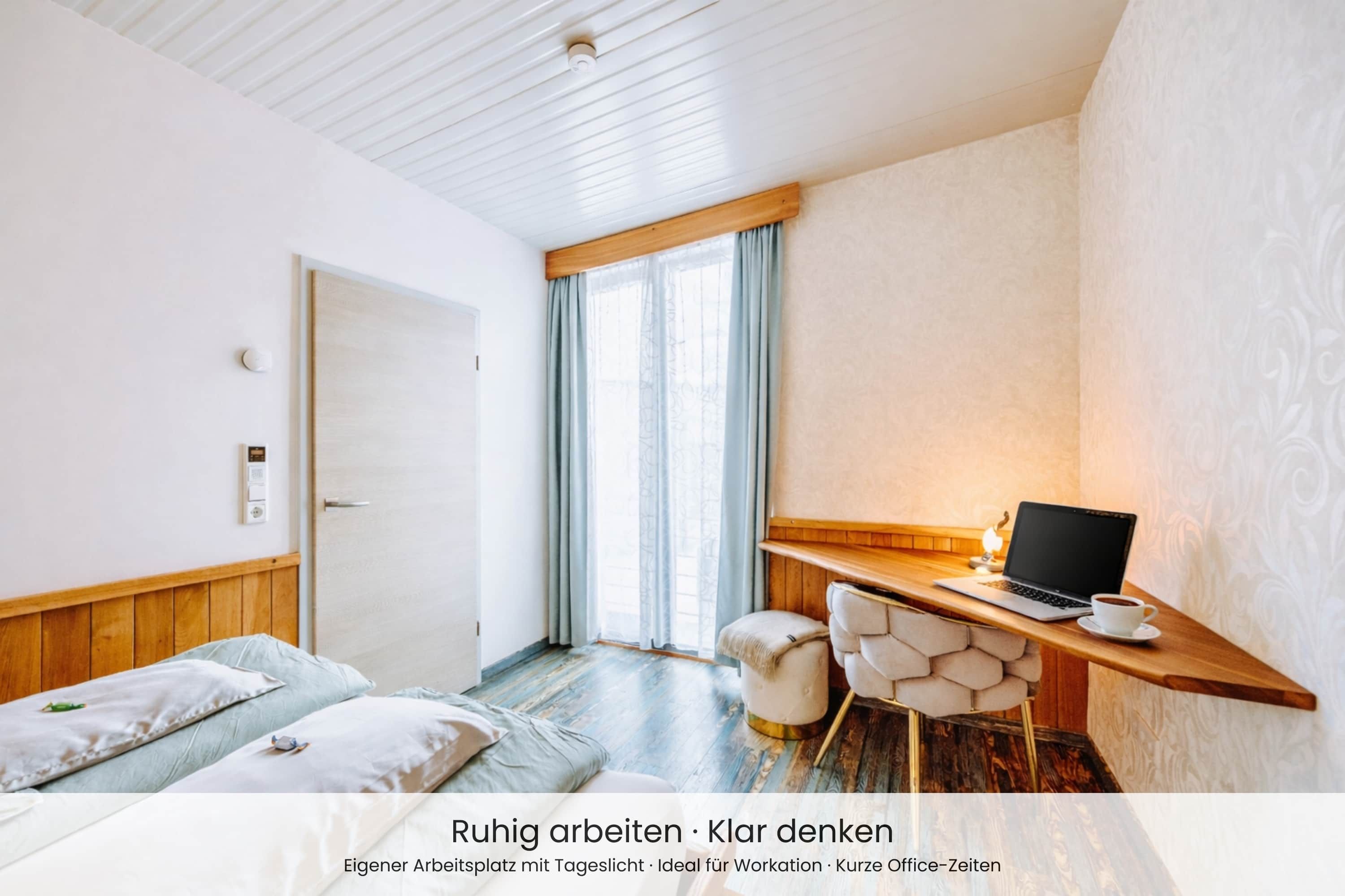Ein modernes Schlafzimmer mit einem Holzbett, einem Schreibtisch mit einem Laptop und Blick ins Freie.