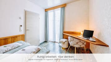 Ein modernes Schlafzimmer mit einem Holzbett, einem Schreibtisch mit einem Laptop und Blick ins Freie.