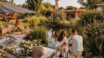 A couple sitting at a table by a pond with a gazebo and lounge chairs in the background.