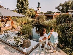 A couple sitting at a table by a pond with a gazebo and lounge chairs in the background.