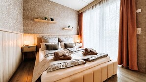 Een slaapkamer met een groot bed, nachtkastjes, een bankje en een raam met gordijnen.