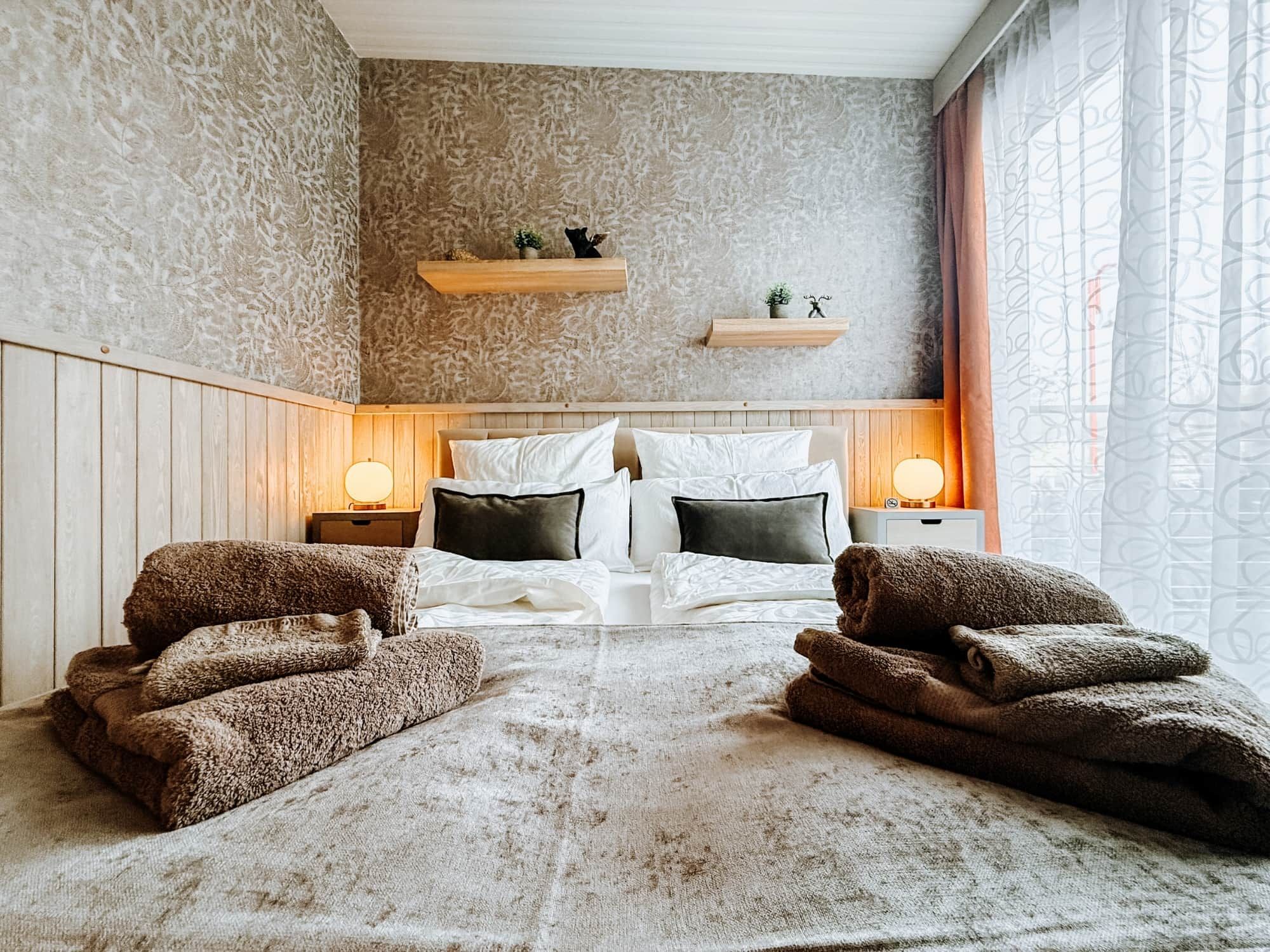 Une chambre à coucher avec un grand lit, deux tables de chevet, une tête de lit en bois et une fenêtre avec des rideaux.