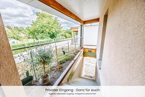 Un balcon donnant sur un jardin, avec un bâtiment visible au loin.