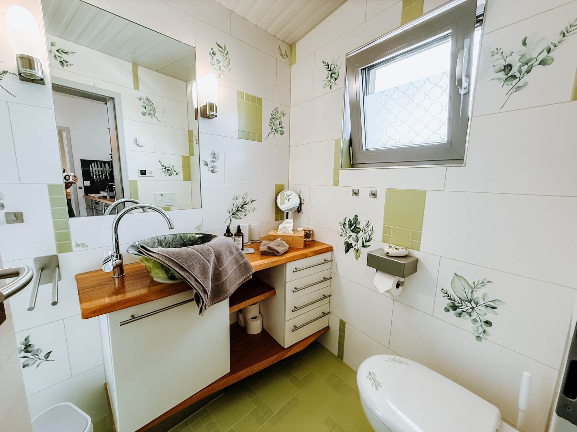 A bathroom with a sink, mirror, toilet, and a window.