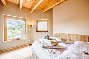 A bedroom with a bed, two windows, a bedside lamp, and a view of greenery.