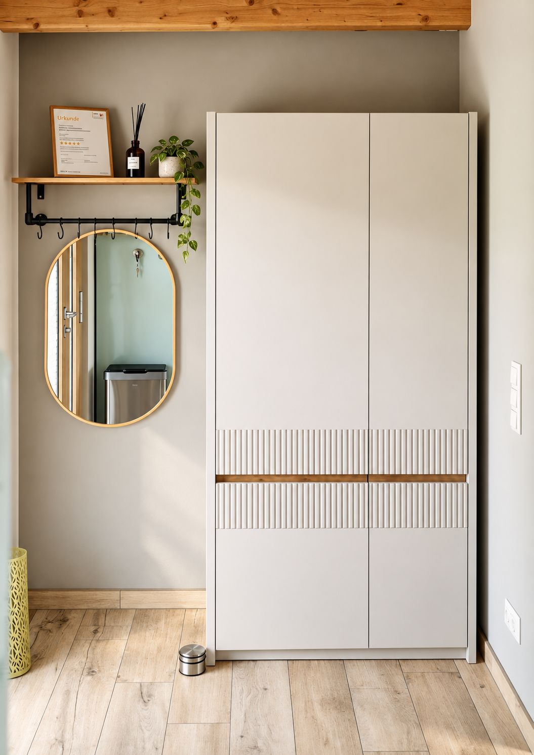 Een kamer met een witte garderobe, een ronde spiegel, een klein plankje met een ingelijst certificaat en een potplant.