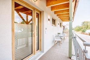 A balcony with a wooden ceiling, a table with chairs, and a view of the surrounding landscape.