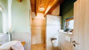 A bathroom with a wooden ceiling, a white sink, a toilet, and a shower area.
