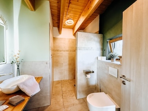 A bathroom with a wooden ceiling, a white sink, a toilet, and a shower area.