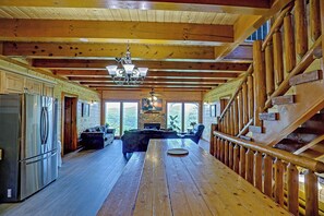 A spacious log cabin interior with a wooden dining table, a kitchen with a refrigerator, a fireplace, and a staircase. - Luxurious Mountain Retreat w/ Theater & Indoor Pool (Sevierville)