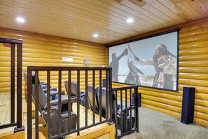 A wooden-paneled room with a projector screen displaying a movie scene, seating area with chairs, and a wooden door. - Luxurious Mountain Retreat w/ Theater & Indoor Pool (Sevierville)
