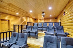 Ein Interieur einer Blockhütte mit mehreren Sitzreihen, einem Projektor und einer Treppe, die in einen oberen Bereich führt.
