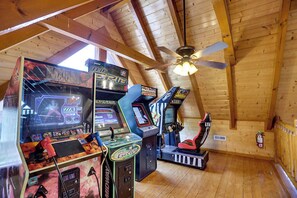A room with wooden ceiling beams, a ceiling fan, and arcade machines. - Luxurious Mountain Retreat w/ Theater & Indoor Pool (Sevierville)