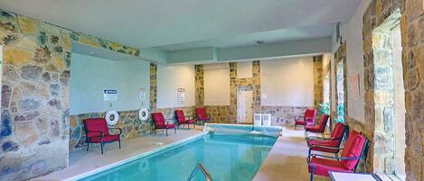 An indoor swimming pool with stone walls, red chairs, and a poolside table.