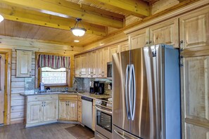 A kitchen with wooden cabinets, stainless steel appliances, and a window with curtains. - Luxurious Mountain Retreat w/ Theater & Indoor Pool (Sevierville)