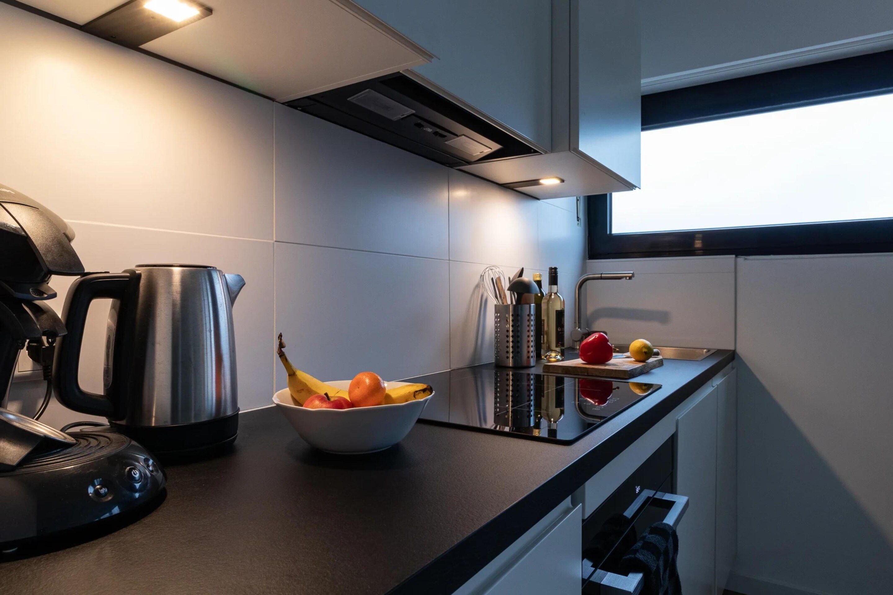 A modern kitchen with a kettle, fruit bowl, and wine bottles on the counter.