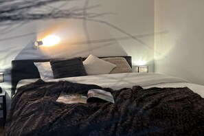 A bed with a dark blanket, pillows, and a magazine. There is a wall-mounted lamp and a small table with a lamp beside the bed. - Luxurious Detached Holiday Home With Valley Views for 8 in Winterberg (Winterberg)