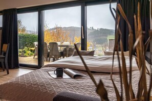 Ein Schlafzimmer mit einem großen Bett, einer Kaffeetasse und Blick auf eine Terrasse mit Stühlen und einem Tisch.