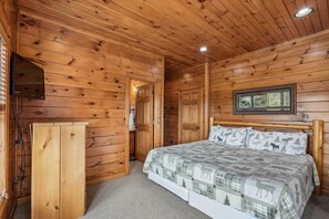 A wooden cabin room with a bed, a television, and a door leading to another room. - 3-Bedroom Cabin w/ Game Room & Hot Tub (Gatlinburg)