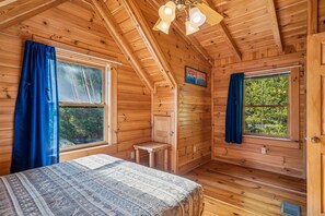 A log cabin bedroom with a bed, two windows, a small table, and a ceiling fan. - Charming Cabin w/ Hot Tub & Fireplace (Sevierville)