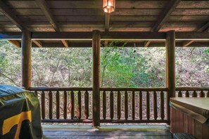 A wooden deck with a railing, a hanging light fixture, and a view of a forested area. - Charming Cabin w/ Hot Tub & Fireplace (Sevierville)