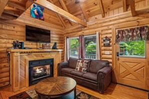 Ein Interieur einer Blockhütte mit Kamin, einer Ledersofa, einem an der Wand montierten Fernseher und einer Tür mit einem dekorativen Schild.