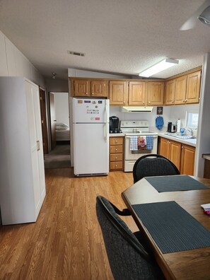 A compact kitchen with wooden cabinets, a white refrigerator, a stove, and a dining area with a table and chairs.