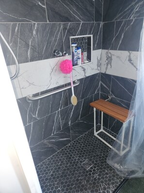 A bathroom with a shower, a bench, and toiletries on a shelf.
