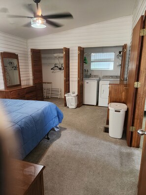 A bedroom with a bed, a dresser, a ceiling fan, a washing machine, and a laundry basket.
