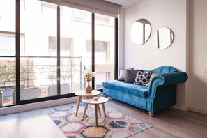 Een moderne woonkamer met een blauwe bank, twee ronde spiegels, een klein tafeltje met een vaas, en een geometrisch vloerkleed.