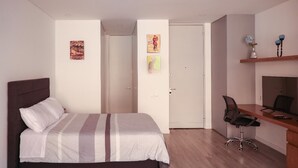 A bedroom with a bed, a desk, and a chair. There are two doors, one leading to another room and another to the outside. - Studio in Unicentro|Santa Barbara|Clinica Santafe (Bogotá)
