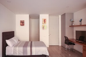 Een slaapkamer met een bed, een bureau en een stoel. Er zijn twee deuren, waarvan er één naar een andere kamer leidt en de andere naar buiten.