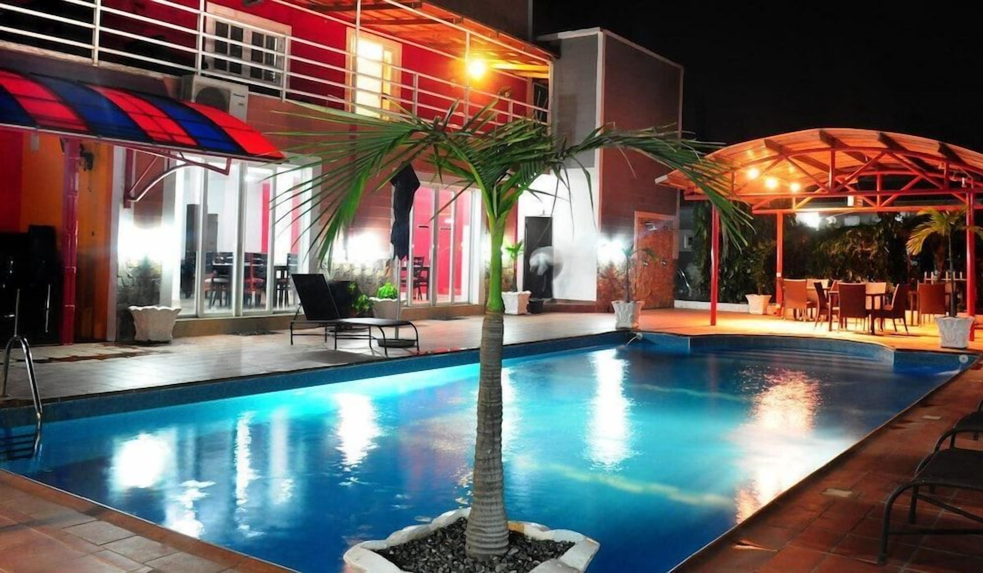 A swimming pool with a palm tree, outdoor seating, and a building with large windows.