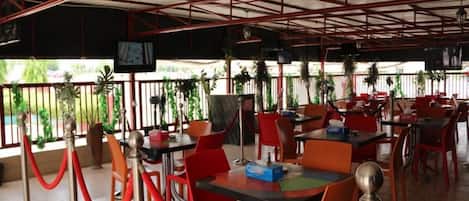 An indoor dining area with tables and chairs, a television screen, and a view of the outdoors.