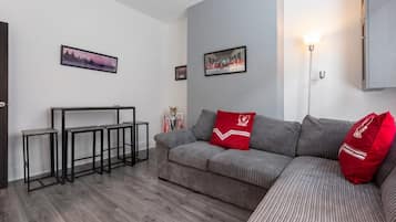 En moderne stue med en grå sofa, røde puder, et sofabord og billeder i rammer på væggen.