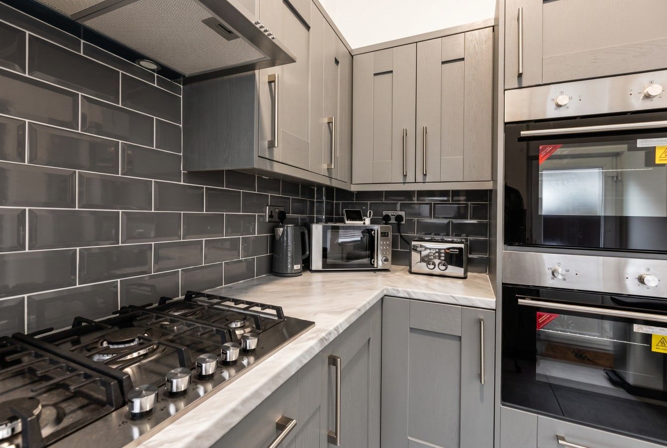 A modern kitchen with grey cabinets, a gas stove, a microwave, and an oven.
