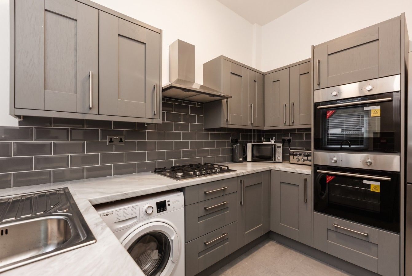 A modern kitchen with grey cabinets, a built-in washing machine, a microwave, and a stove.