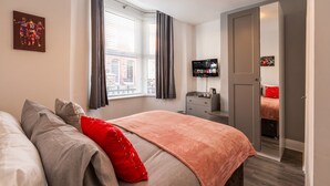 Ein Hotelzimmer mit einem Bett, einem Fernseher, einem Kleiderschrank und einem Fenster mit Vorhängen.