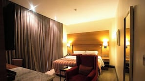 Una habitación de hotel con una cama, un sillón rojo, una mesita y un cabecero de madera.